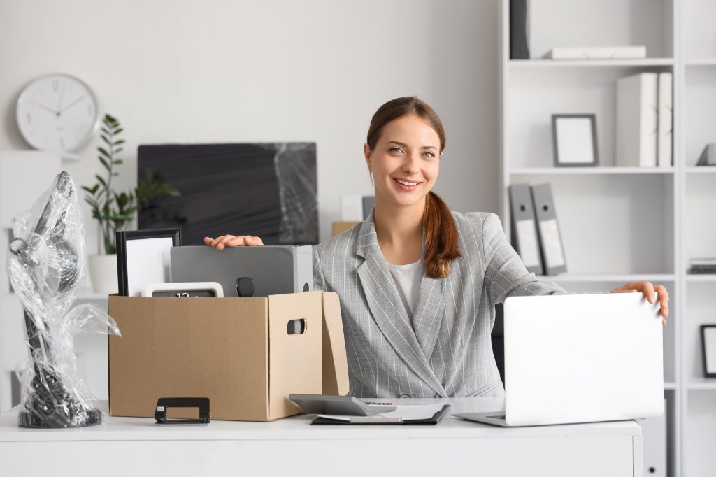 Happy young businesswoman with a laptop and cardboard